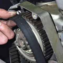 Dłoń mechanika sprawdza stan paska rozrządu, który jest kluczowym elementem silnika.