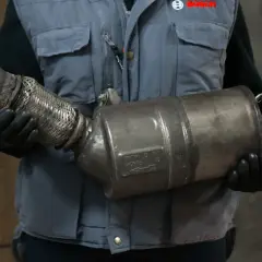 Mechanik w rękawiczkach trzyma zużyty filtr cząstek stałych.
