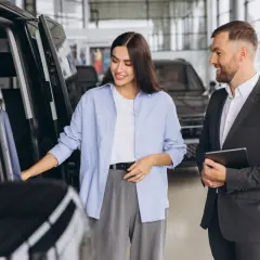 Kobieta ogląda samochód w salonie, sprzedawca z tabletem oferuje leasing bezpośredni.