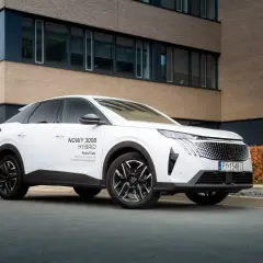 Biały Peugeot 3008 hybryda plug-in zaparkowany przed nowoczesnym budynkiem.