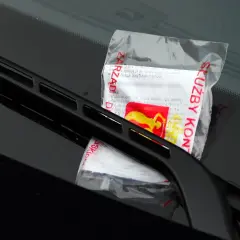 Mandat za parkowanie leży pod wycieraczką. Dokument z czerwonymi napisami "ZARZĄD" i "SŁUŻBY KON" informuje o karze.