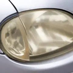 Żółta, zmatowiona lampa samochodowa przed polerowaniem. Widać wyraźną różnicę między zmatowioną częścią a tą, która została już poddana polerowaniu.