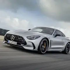 Srebrny Mercedes-AMG GT 63 sunie po torze wyścigowym, chmury na niebie podkreślają dynamikę jazdy.
