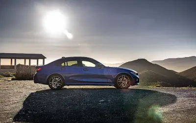 Niebieskie BMW 318d na tle górskiego krajobrazu o zachodzie słońca.