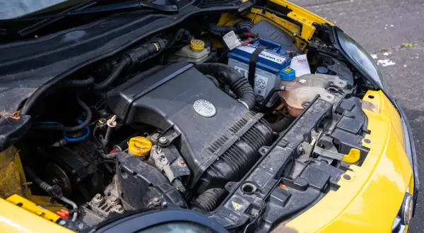 Silnik żółtego Alfa Romeo MiTo. Widoczny akumulator, obudowa filtra powietrza z logo marki i płyny eksploatacyjne.