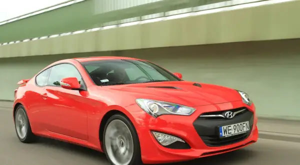 Czerwony Hyundai Genesis Coupe pędzi pod zielonym wiaduktem.