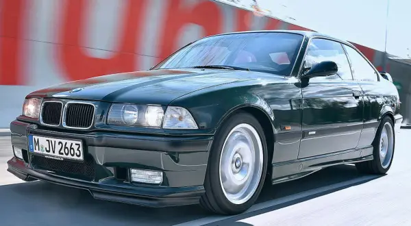 Klasyczne BMW E36 w kolorze ciemnej zieleni pędzi po drodze.