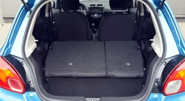 Błękitny Mitsubishi Space Star z otwartym bagażnikiem. Widoczne złożone tylne siedzenia, tworzące płaską przestrzeń ładunkową.
