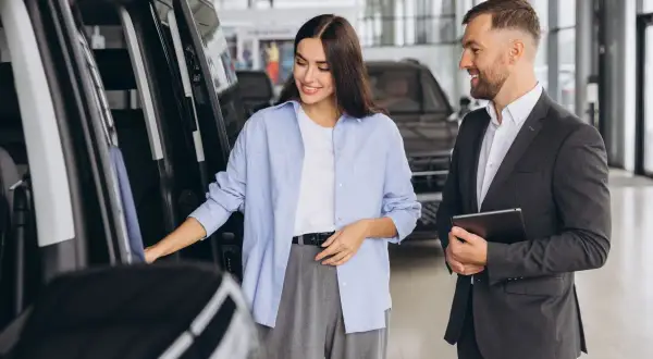 Kobieta ogląda samochód w salonie, sprzedawca z tabletem oferuje leasing bezpośredni.