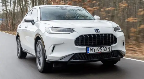Biały Honda ZR-V jedzie po drodze wśród drzew.