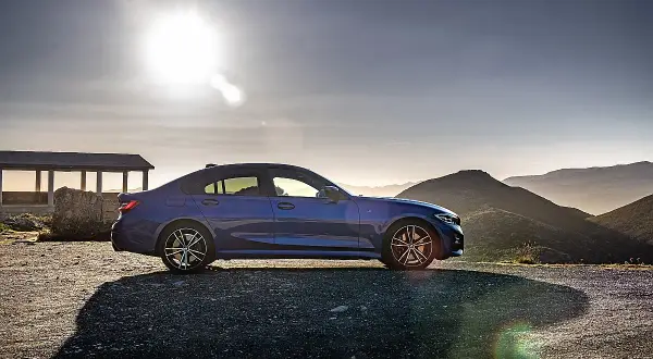 Niebieskie BMW 318d na tle górskiego krajobrazu o zachodzie słońca.