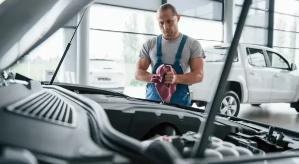 Mechanik z ręcznikiem przy silniku. Rozważasz naprawa samochodu w leasingu a koszty? Sprawdź, co obejmuje umowa.