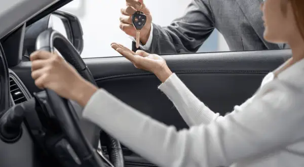 Kluczyki do nowego auta przekazuje sprzedawca, a klientka zastanawia się: leasing czy gotówka?