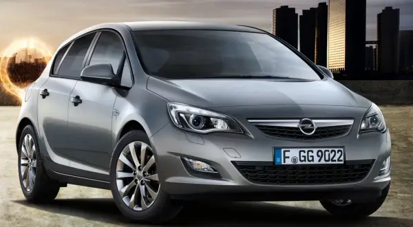 Srebrny Opel Astra J z nowoczesnymi światłami i felgami stoi na tle miejskiej panoramy.
