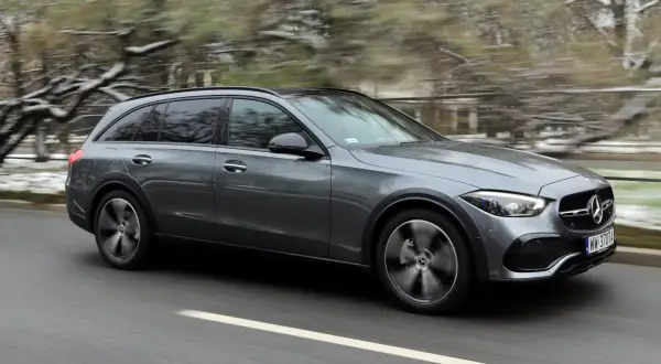 Szary Mercedes All-Terrain z napędem 4matic pędzi po drodze, zaśnieżone drzewa w tle.