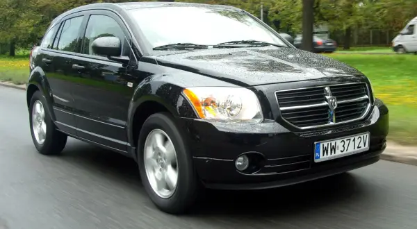 Czarny Dodge Caliber jedzie po mokrej drodze.