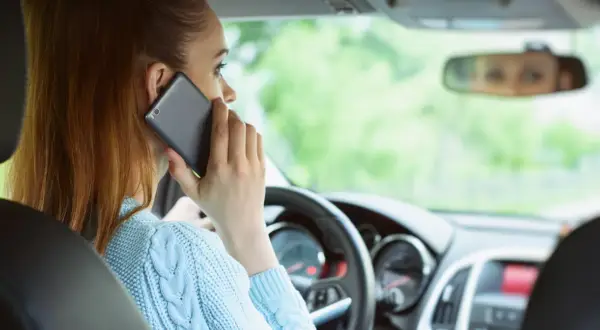 Kobieta rozmawia przez telefon podczas jazdy samochodem, ignorując drogę.