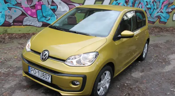 Żółty Volkswagen up! zaparkowany pod kolorowym graffiti.