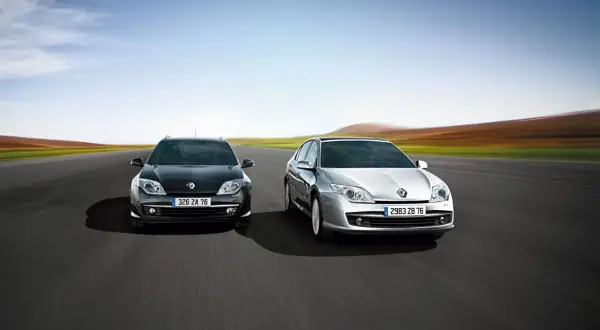 Dwa modele Renault Laguna 3, czarny i srebrny, pędzą po pustej drodze na tle rozmytego krajobrazu.