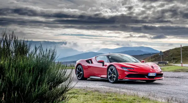 Czerwone Ferrari SF90 na tle gór i burzowego nieba.