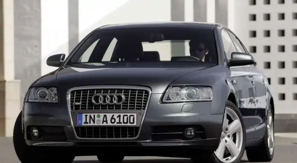 Elegancki, ciemnoszary Audi A6 C6 z przyciemnianymi szybami i chromowanymi felgami, zaparkowany przed nowoczesnym budynkiem.