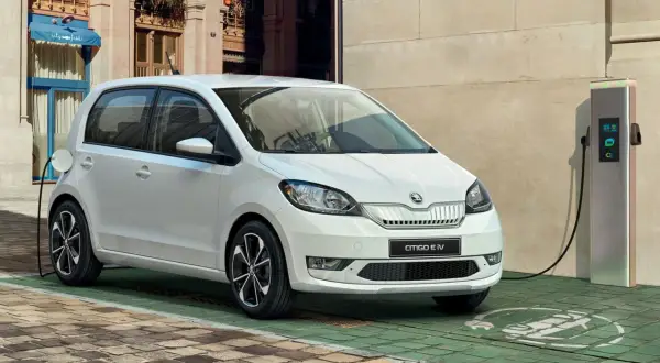 Biały Skoda Citigo e IV ładuje się przy stacji ładowania na brukowanej uliczce, gotowy na miejskie przygody.