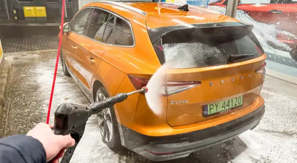 Pomarańczowy Skoda Enyaq jest myty na myjni bezdotykowej. Woda pod ciśnieniem spływa po karoserii, tworząc pianę.