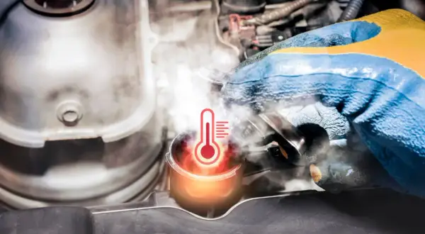 Para mechanika w rękawicy próbuje otworzyć korek chłodnicy, z którego wydobywa się para. Widoczny symbol termometru wskazuje na **wysoką temperaturę płynu chłodniczego**.