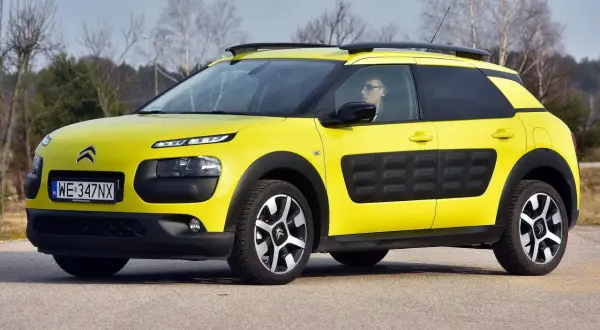 Żółty Citroen Cactus z czarnymi wstawkami na drzwiach i relingami dachowymi, zaparkowany na drodze.