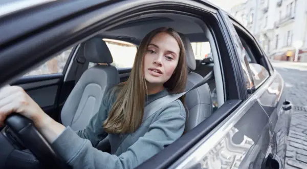 Młoda kobieta, współwłaściciel samochodu poniżej 25 roku życia, prowadzi auto po brukowanej ulicy.