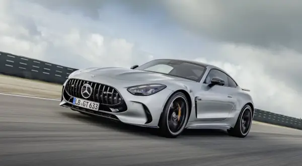Srebrny Mercedes-AMG GT 63 sunie po torze wyścigowym, chmury na niebie podkreślają dynamikę jazdy.