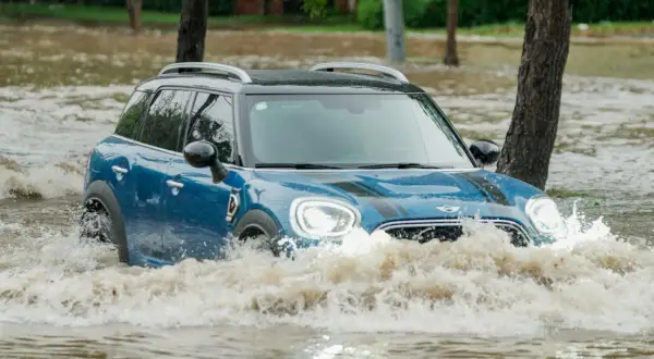 Niebieski Mini Cooper przedziera się przez powódź. Ubezpieczenie GAP przy zakupie za gotówkę chroni przed stratami w takich sytuacjach.