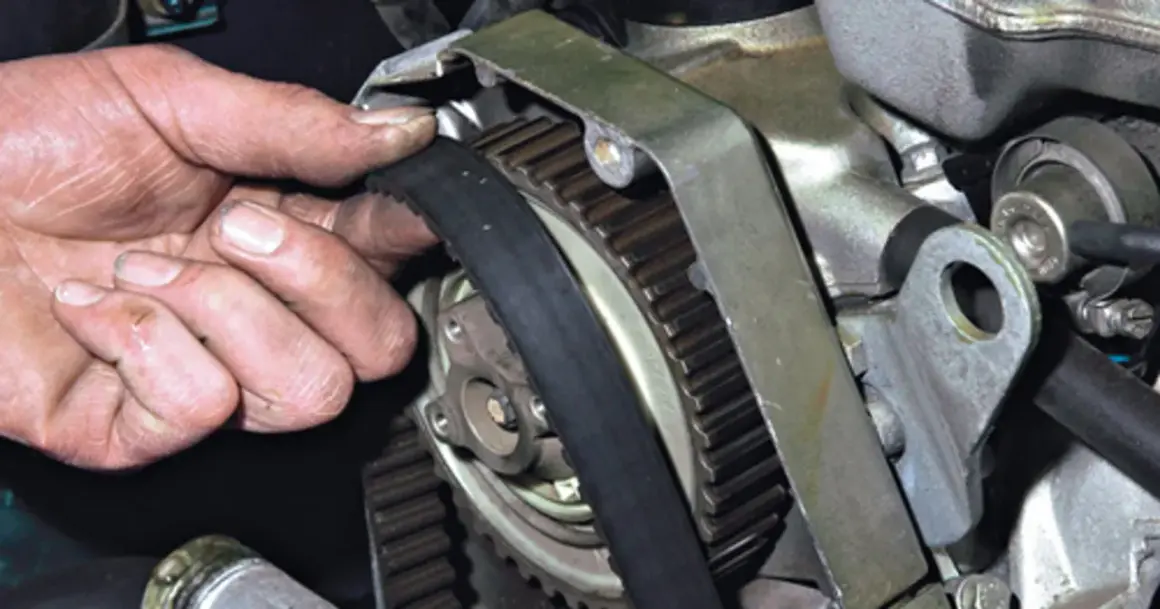 Dłoń mechanika sprawdza stan paska rozrządu, który jest kluczowym elementem silnika.