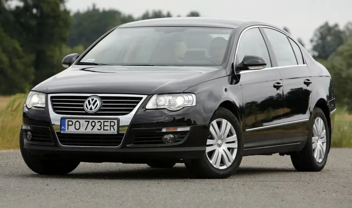 Czarny Passat B6 z polskimi tablicami PO 793ER na tle zieleni.
