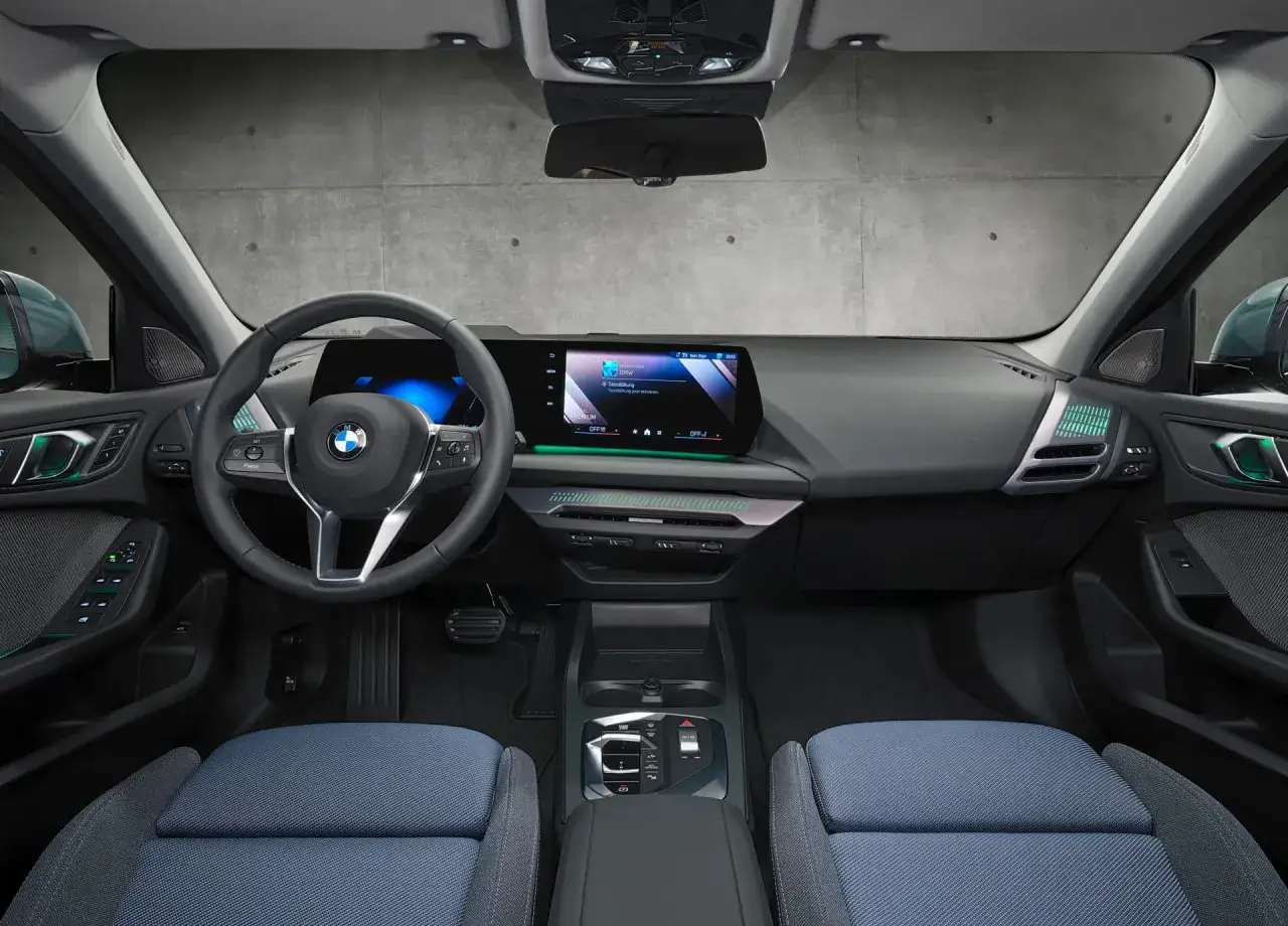 Wnętrze BMW Seria 1: nowoczesny kokpit z dużym ekranem, kierownicą i niebieskimi fotelami.