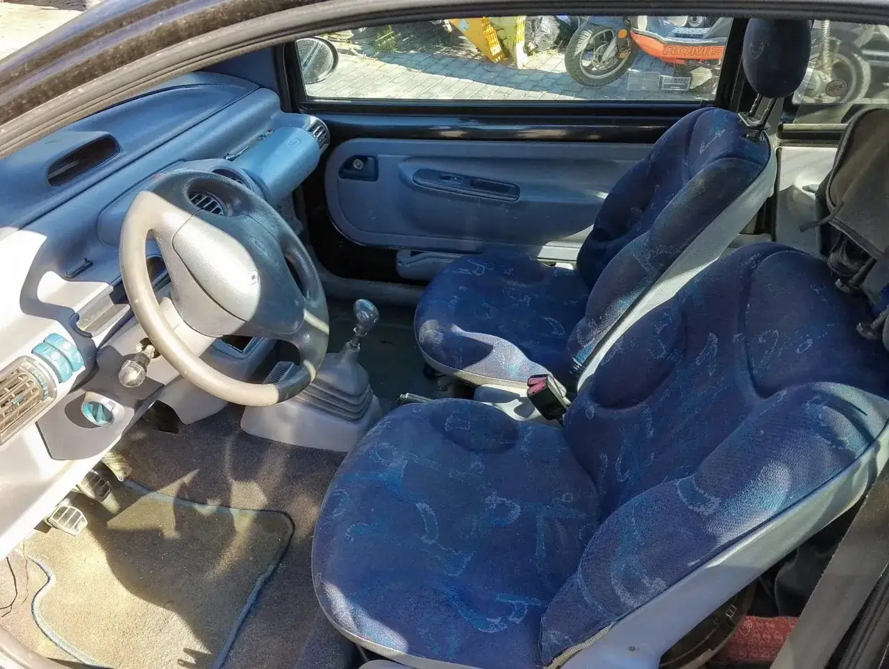 Wnętrze Renault Twingo z niebieskimi siedzeniami i charakterystyczną kierownicą.