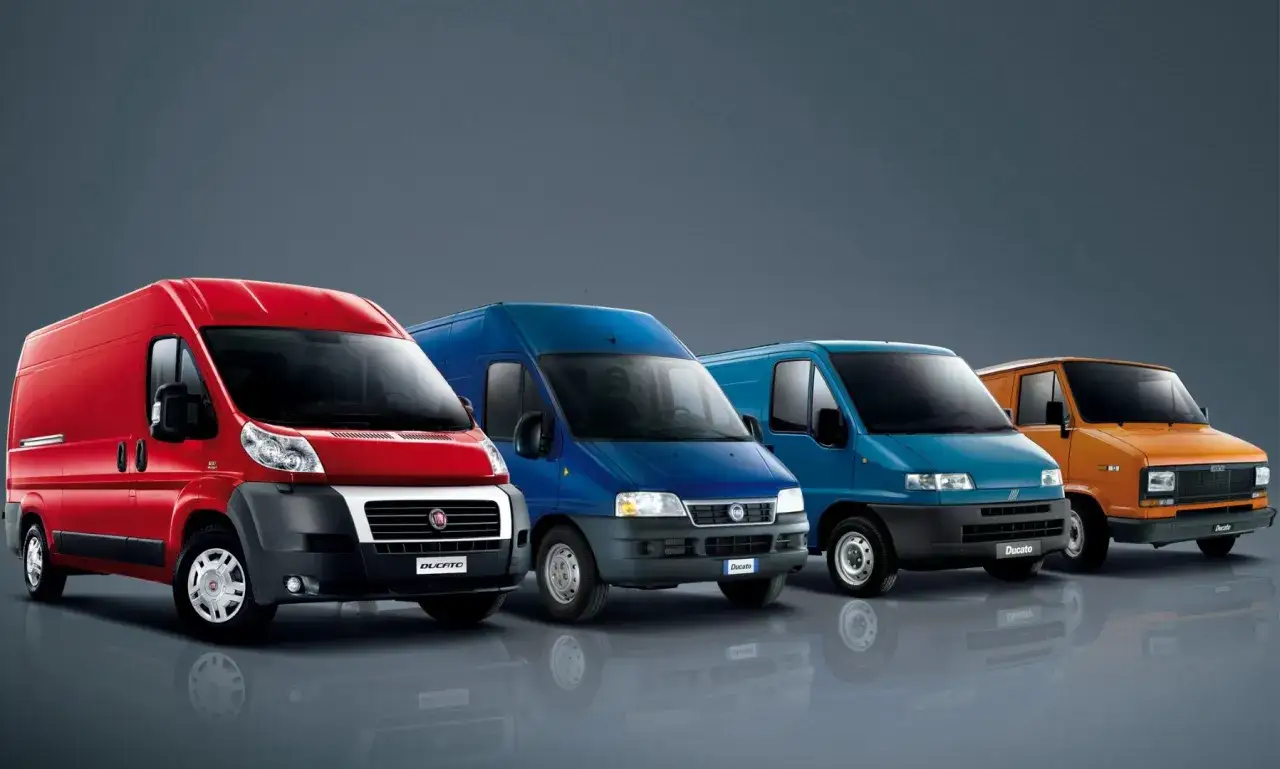 Cztery furgonetki Fiat Ducato w różnych kolorach: czerwonym, dwóch odcieniach niebieskiego i pomarańczowym, stoją obok siebie.