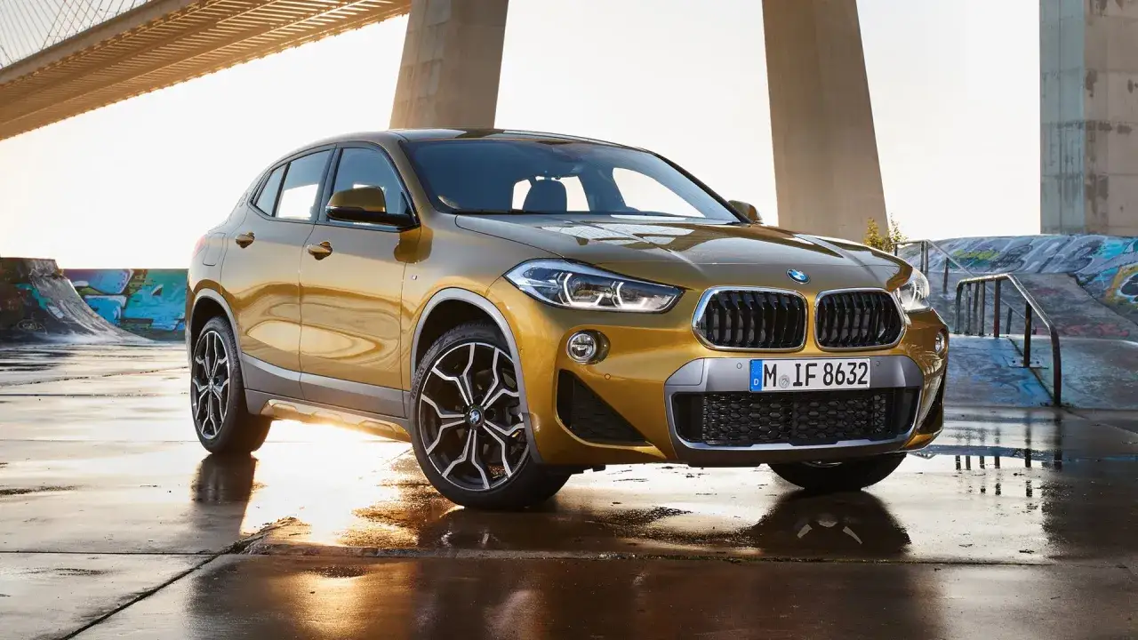 Złoty BMW X2 na mokrej nawierzchni, pod mostem. Idealny wybór dla tych, którzy szukają nowoczesnych aut w abonamencie.