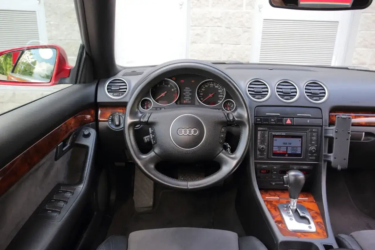 Wnętrze Audi A4 B6 z drewnianymi wstawkami i czarną kierownicą. Widoczny panel radia i nawigacji.