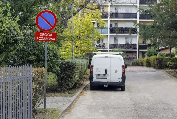 Znak "zakaz zatrzymywania się" i "droga pożarowa" obok białego vana. Kierowca może spodziewać się mandatu za złe parkowanie od straży miejskiej.