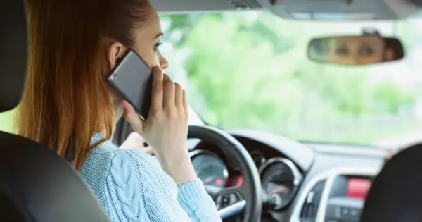 Kobieta rozmawia przez telefon podczas jazdy samochodem, ignorując drogę.