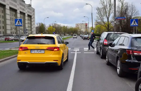 Mężczyzna przechodzi przez pasy, podczas gdy samochody blokują przejście dla pieszych. Żółty Audi stoi na pasach.